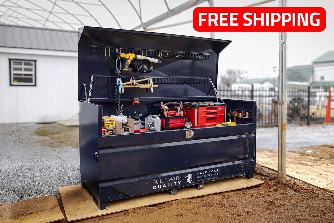 A large, industrial storage container known as Quick-E-BARBoxx, which is black in color, is open and showing various tools and equipment organized inside it. The container is placed outdoors on a wooden palette, and there is a building in the background.