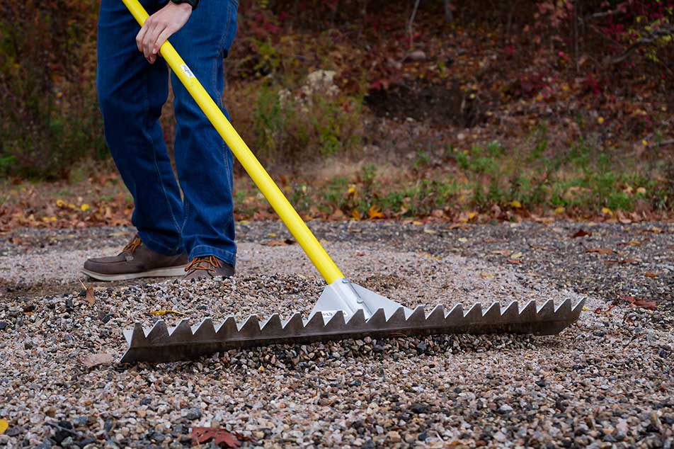 Person using a garden rake with a yellow handle on a gravel surface